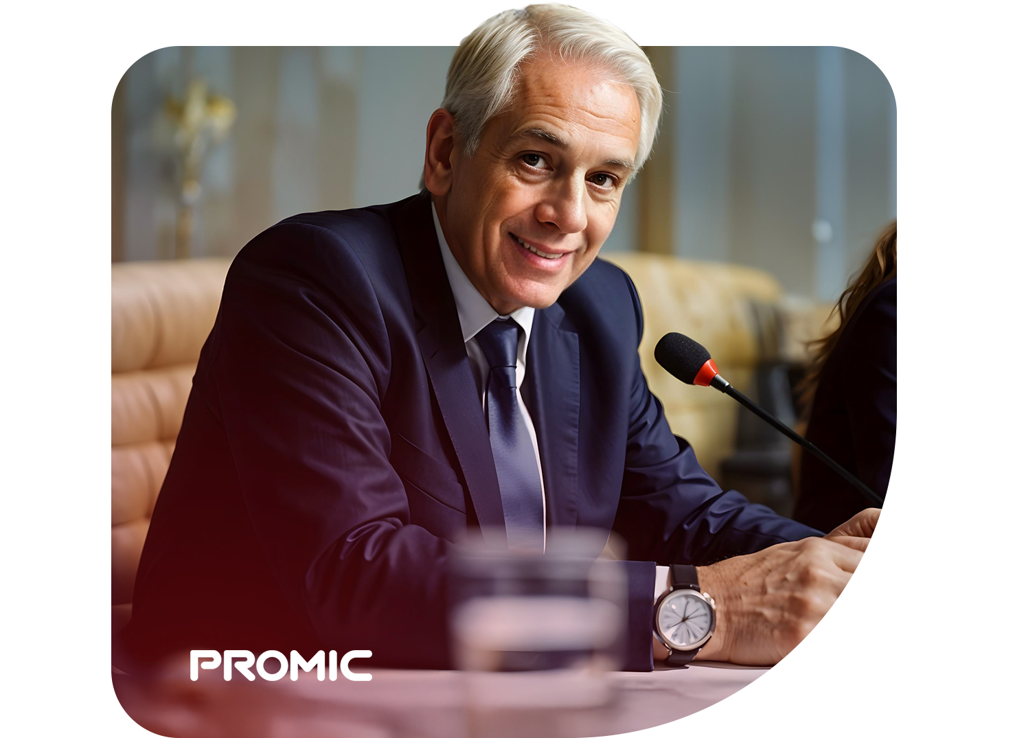 Homem de terno em plenário, sentado diante de microfone gooseneck. Logo Promic, produto da Riole, no canto inferior esquerdo.