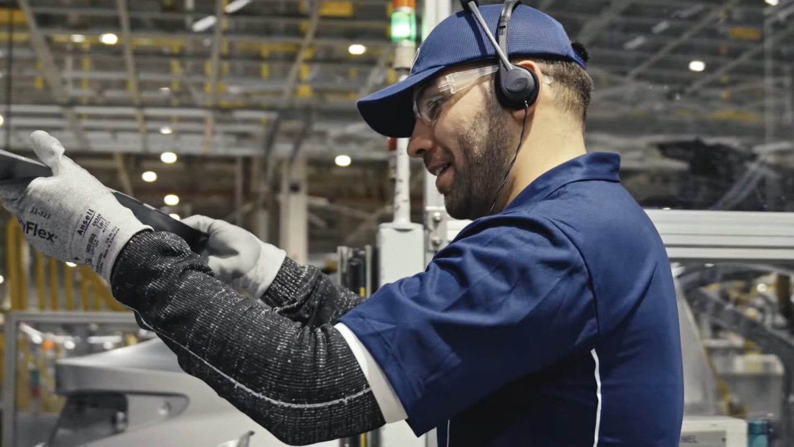 Homem durante Programa de Visitas Guiadas na Fábrica da Hyundai usa headset HE2B da Riole enquanto manuseia peça de carro.