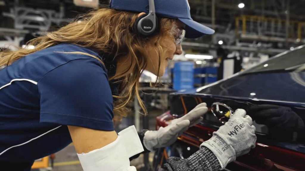 Mulher participa de visitas guiadas na fábrica. Usa equipamentos WalkMeet, da Riole, enquanto cola emblema no carro.