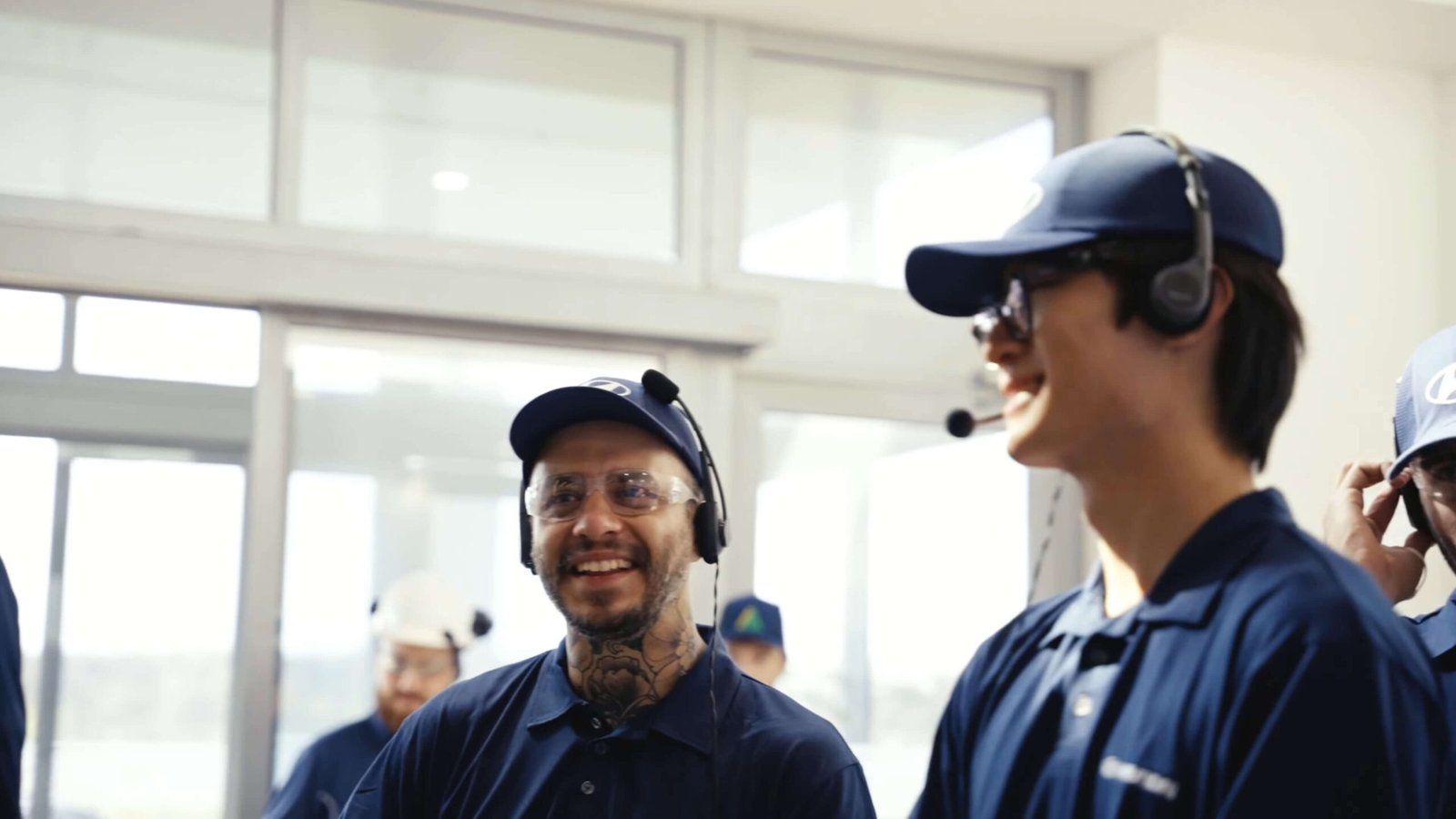 Dois homens usam uniformes e bonés da Hyundai, WalkMeet da Riole e óculos de proteção durante visitas guiadas na fábrica.