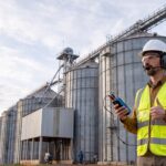 Profissional de segurança em unidade de armazenamento de grãos com silos ao fundo